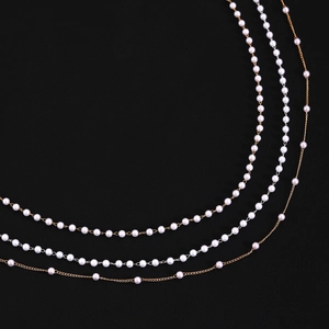 Détail d'un collier de perles blanches multicouche avec fine chaîne dorée sur fond noir