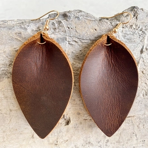 Brown crazy horse leather leaf earrings with gold hooks on a rustic stone background