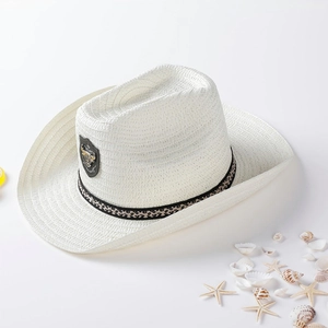 White straw cowboy hat with ethnic band and metal bull logo on a beach-themed background