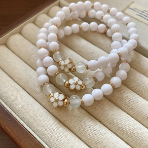 Detailed macro view of a 3-piece set of white beaded floral bracelets with gold accents