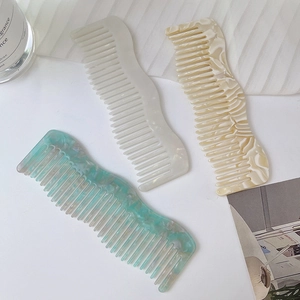 Three wavy cellulose acetate hair combs with marble patterns in cream, beige, and green