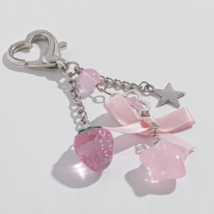Detail of pink strawberry and star charms keychain with silver heart clasp on white background
