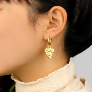 Detail of 18K gold-plated heart earring with relief texture worn on ear