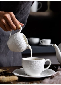 Detail of milk pouring into a white ceramic coffee cup with Baroque relief patterns
