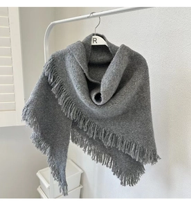 Detail of grey knitted wool shawl with tassel fringe hanging on a minimalist white hanger