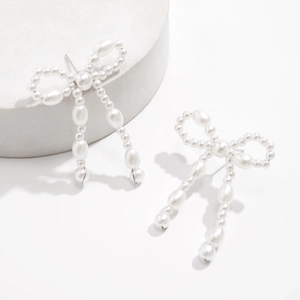 Close-up of pearl bow earrings with fringe design on a minimalist white pedestal