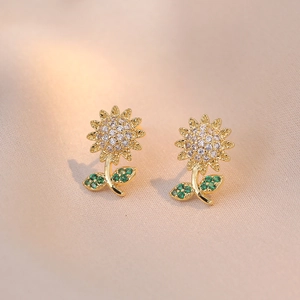 Golden sunflower stud earrings with sparkling white and green zircon on beige silk fabric