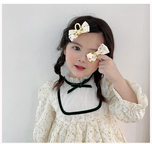 Detail showing a pair of beige polka dot bow hair clips worn on long brown hair