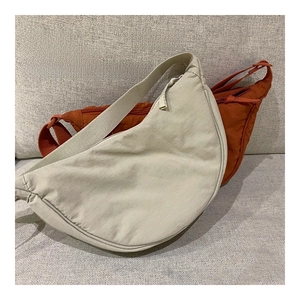 Detail view of nylon crescent bags in off-white and brick red on a grey sofa background