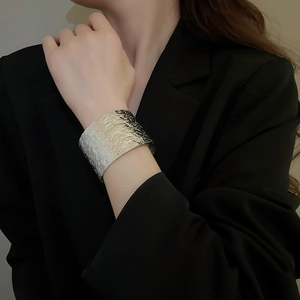 Macro shot of a silver-toned wide cuff bracelet with irregular hammered metal textures