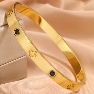 Detail of gold titanium steel bangle featuring black stones and clover patterns on silk