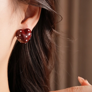 Close-up of red heart earrings with white polka dots worn on a model's ear
