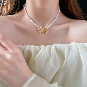 Close-up of elegant pearl necklace with gold floral pendant on model's neckline