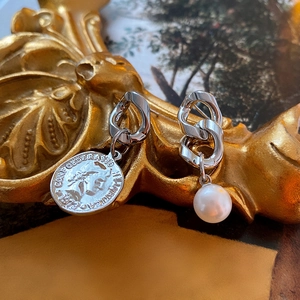 Detail of asymmetric silver earrings with portrait coin and white pearl on vintage background