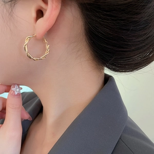 Detail of twisted gold hoop earrings featuring woven metal texture on a model