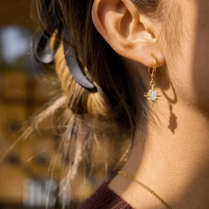 Golden North Star earrings with white opal stone and rhinestones worn by a model