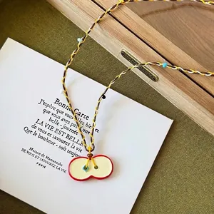 Detail of red apple pendant with colorful braided cord and 65cm length measurement