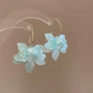 Détail des boucles d'oreilles fleurs en résine bleu clair avec crochets dorés et fini perlé