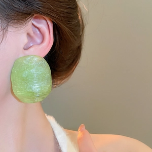Close-up of translucent green irregular disc earrings with a brushed texture on model