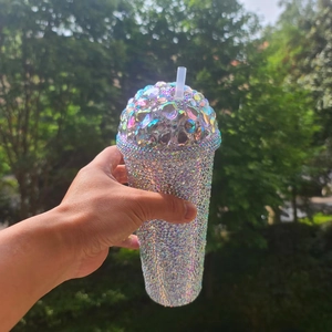 Sparkling silver rhinestone double-wall tumbler with straw held in hand outdoors