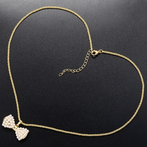 Makroaufnahme einer goldenen Schleife mit Perlen auf herzförmiger Kette vor schwarzem Grund