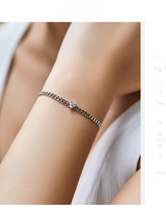Macro detail of a 925 silver curb chain bracelet with a heart-shaped crystal on the wrist