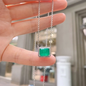 Detail of square emerald pendant necklace worn on neck with small diamond halo accents