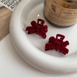 Close-up of small wine red velvet bow hair clips on a decorative white porcelain plate