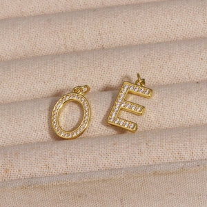 Detailed close-up of zircon-inlaid letter O and E pendants on beige fabric texture