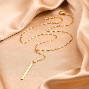 Detail view of gold Y-necklace with long rectangular pendant on silk fabric