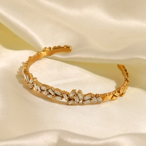 Bracelet jonc ouvert doré élégant serti de zircons posé sur un tissu en soie beige