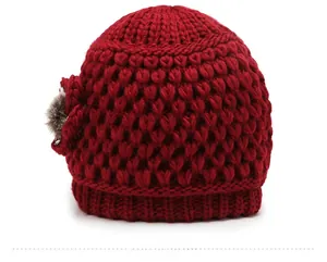 Detailed side view of a thick red knitted hat with a floral accent and small pom-pom