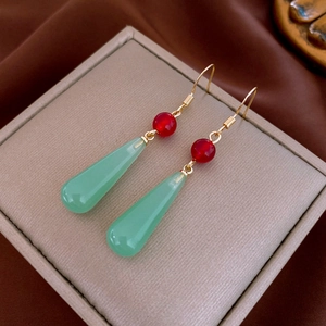 Macro detail of vintage gold earrings with red round beads and green teardrop pendants