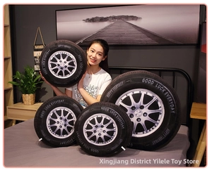 Detail showing four sizes of 3D tire plush pillows with silver hub design on a cozy bed