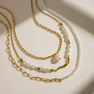 Layered gold-plated stainless steel necklace set with freshwater pearls on beige backdrop