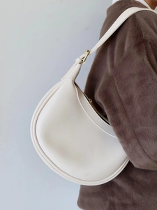 Detail view of cream crescent leather bag with gold buckle on shoulder strap