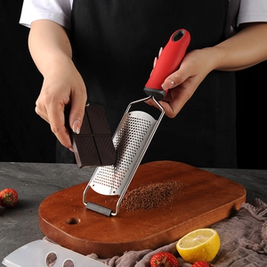 Stainless steel cheese grater with red handle being used to grate dark chocolate