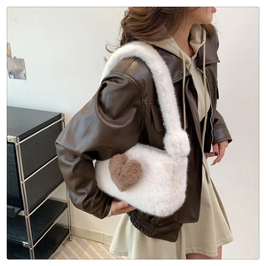 Detailed view of white faux fur shoulder bag with a brown heart plush charm on a model
