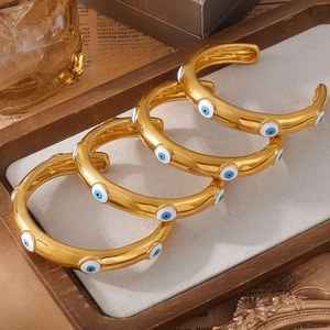 Gold plated stainless steel evil eye open bangles with blue enamel accents in a tray