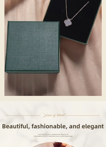 Detail view of a four-leaf clover pendant necklace inside a green linen gift box