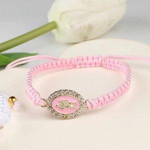 Detail of pink woven bracelet featuring a gold Madonna charm with white crystals