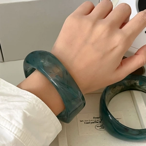 Close-up of deep green marble resin bangle on a wrist with white linen shirt sleeve