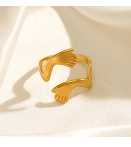 Detail shot of gold-plated stainless steel hugging hands ring on white silk background