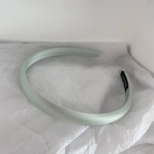 Detail of light green satin headband featuring a black handmade textile label on the side