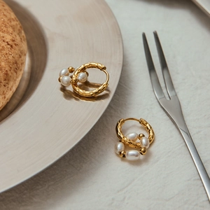 Detailed close-up of golden hoop earrings with hammer-textured finish and white pearls