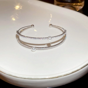 Close-up of double-layer silver bangle with sparkling zircons and white pearls in a dish