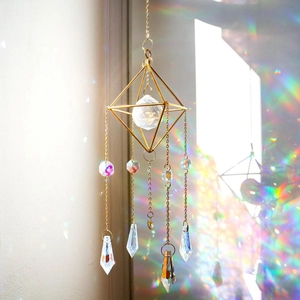 Détail d'un attrape-soleil géométrique doré avec sphère en cristal et reflets arc-en-ciel