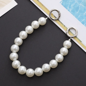 Detail view of white pearl handbag chain with silver metal spring clasps on black background