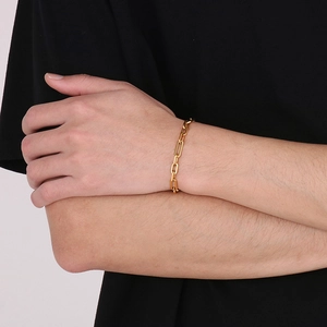 Gold stainless steel paperclip link bracelet worn by a person on a dark sleeve