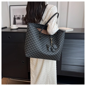 Detail of black monogram tote bag on shoulder featuring removable dog-shaped charm